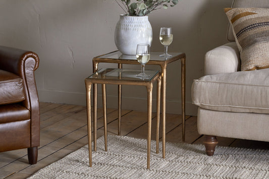 Pair of Nkuku Gilasi cast metal and glass nesting side tables in antique brass finish, set of 2 with sleek modern design.