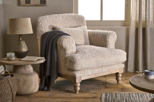 Off-white Otas Teddy cotton armchair by Nkuku, showcasing plush textured upholstery and a cozy armchair design in a natural setting.